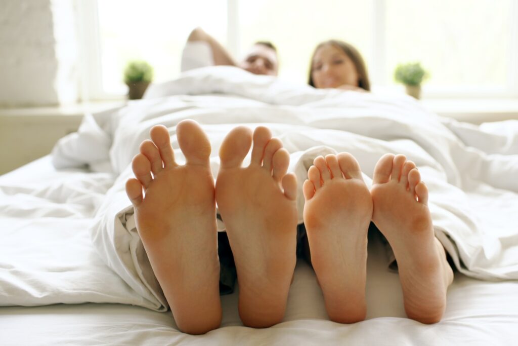 Closeup of young beautiful and loving couple play and dance their feet while wake up in bedroom in morning
